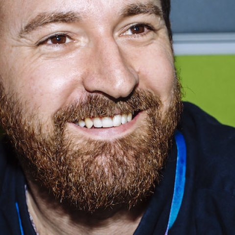 bearded man wearing a dark blue shirt and smiling